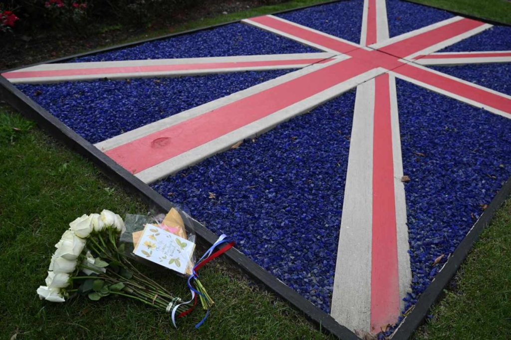 A bouquet of flowers is placed next to a British flag outside the British Embassy in Washington, DC, on September 8, 2022, following the death of Queen Elizabeth II. Queen Elizabeth II, the longest-serving monarch in British history and an icon instantly recognizable to billions of people around the world, has died aged 96, Buckingham Palace said on Thursday. (Photo by SAUL LOEB / AFP)